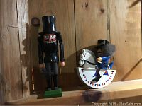 Two wooden nutcracker toys displayed on a wooden wall shelf, soldier on horse and chimney sweep.