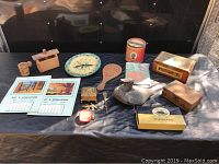 General overview of 16 vintage and antique collectibles including woodenware, advertising tins and boxes, wall clock, and a duck decoy on dark fabric surface.