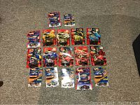 Group photo of 17 unopened NASCAR diecast cars in original packaging including 8 Hot Wheels and 9 Racing Champions. Cars are arranged on floor, packaging mostly red and blue with racing graphics.