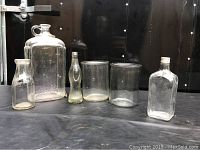 Six clear glass bottles including Rockdale Dairy Kingston milk bottle and others.