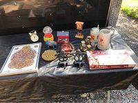 Overview of 14 mixed collectible and vintage items on black cloth, includes German steins, Scrabble, gumball machine, figurines, art, piggy bank, purse, clock.