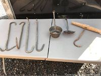Five metal hooks and two vintage metal kitchen tools (scoop and ladle) displayed on a table.