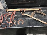 Photo of horse tack items including leather bridle, wooden yoke, horseshoe, and leather straps laid on black surface