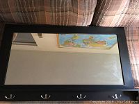 Front view of rectangular mirror with chocolate wood-style frame, shelf along the bottom, and four metal hooks.