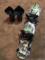 Full view of black Morrow snowboarding boots and Firefly snowboard on carpet.