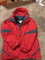 Full red jacket laying open showing the outer layer with grey reflective stripes on sleeves and bottom.
