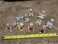 Top view of 10 ceramic faerietots figurines arranged on carpet with measuring tape showing size approximately 3-4 inches tall.