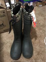 Front view of pair of black rubber Kamik boots with camouflage padded collar and drawstring.