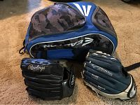 Photo showing two youth baseball gloves (Rawlings black and Mizuno blue) with blue and black Easton equipment bag behind them.