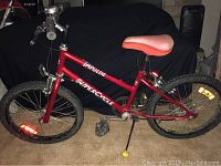 Side view of the complete red Impulse SuperCycle youth bicycle showing frame, chain, pedals, saddle and handlebar.