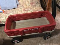 Overview photo of red plastic child's wagon with high side walls, gray base, four black wheels, and "Radio Flyer" logo on side.