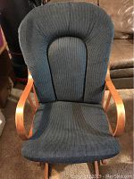 Front view of the blue-gray cushioned glider rocking chair showing padded seat and backrest with wood armrests.