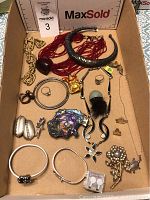Overview of assorted vintage jewelry lot including rings, bracelets, bangles, necklaces, and brooches in a cardboard box