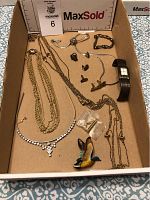 Full photo overview of all jewelry items in a cardboard box including necklaces, cuff links, brooch, and wristwatch.