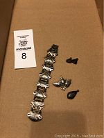 Full view of sterling silver bracelet with hinged links, earrings, brooch, and pendant arranged on a brown background.