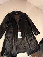 Full view of black leather women's coat with buttons open and showing quilted lining, size tag visible