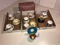 Three cardboard trays containing assorted teacups and saucers arranged side by side on white surface