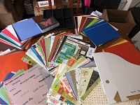 Lot of assorted scrapbooking papers in various colors and sizes along with stickers and small organizer boxes.