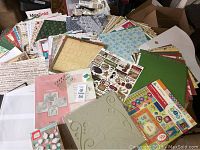 Top-down view of scrapbooking supplies spread on a table showing multiple sheets of patterned paper, sticker sheets, stamp sets, and embellishments.