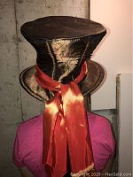 Back view of the shiny dark bronze Mad Hatter top hat with large orange satin ribbon bows tied at the back.