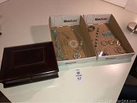 Jewelry box with hinged lid placed next to two boxes containing assorted jewelry items.