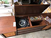 Full view of vintage wooden cabinet showing hinged top open revealing turntable and radio dials, some wear visible on wood.
