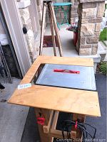 Full view of the homemade saw table showing wooden top with embedded saw and tripod behind.