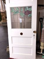 Full view of white door with stained glass panel showing floral and leaf design and wear.