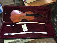 Violin and bow placed inside red velvet-lined violin case.