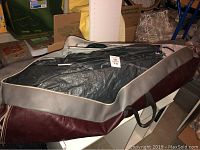 Tent packed inside a large carrying bag with maroon and grey accents, situated on a table in indoor setting.