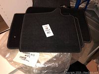 Set of four black car floor mats stacked on top of each other, showing overall condition and texture.