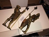Two brass knight wall decorations on a white surface. Both hold shields and pole weapons, showing full body and detail of armor.