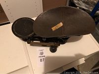 Full view of antique balance scale showing larger oval pan and smaller round pan, with weight markings on arm.