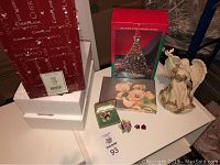 Photo of the lot items including boxed musical Christmas tree, Sarah's Angel figurine, floral jewelry box with brooch and earrings, and vintage floral book or card.