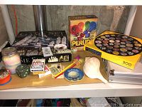 Overall view of games on table including puzzle box, Perudo dice game, Hoyle cards, glass game set, poker case, candle jar, small dice cup and decorative items.
