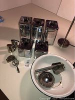 Photo showing vintage steel tins for flour, sugar, coffee, tea, plus salt and pepper shakers and white enamel basin with kitchen tools inside