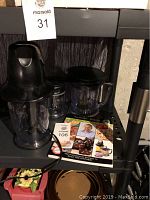Front view of the black Ninja blender base with attached pitcher, lid, blades, and the Ninja recipe book spread out on a metal cart.