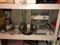 Shelf with Oster push button blender, Henckel frying pan, and boxed 3-tier spice rack