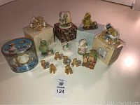 Multiple Cherished Teddies figurines arranged on a surface, some on original boxes with vintage labels. Variety of teddy bear scenes in various costumes.