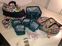 Various Thirty One storage and makeup bags displayed on a white surface, showing assortment of fabric patterns and sizes.