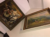 Two paintings photographed angled; Man playing instrument on left, deer landscape on right.