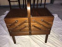 Closed view of the wooden sewing box showing its handle, four legs, and expandable sectional design with brass hardware.