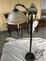 Full view of the floor lamp showing complete height, metal curved arm with decorative elements, and glass shade.