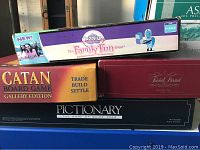 Four board games stacked: Cranium, Catan Gallery Edition, Trivial Pursuit Baby Boomer Edition, and Pictionary.