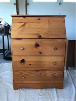 Closed pine drop front bureau showing three drawers and brass knobs.