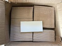 Box containing tightly stacked matte white subway tiles arranged in four compartments.