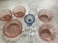 Photo showing collection of rose-colored glass bowls, clear wine glasses, and a blue textured glass, all arranged on white surface, no visible chips or cracks.