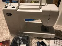 Photo showing the Kenmore sewing machine with power cord, black foot pedal, manual, and thread spools, placed on a beige carpet.