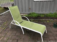 Green adjustable outdoor lounger with steel frame and fabric seat on a brick patio, showing some rust spots.