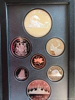 Photo showing seven 1986 Canadian proof coins arranged in display case, including a large silver-colored locomotive dollar coin and other denomination coins depicting various Canadian symbols.